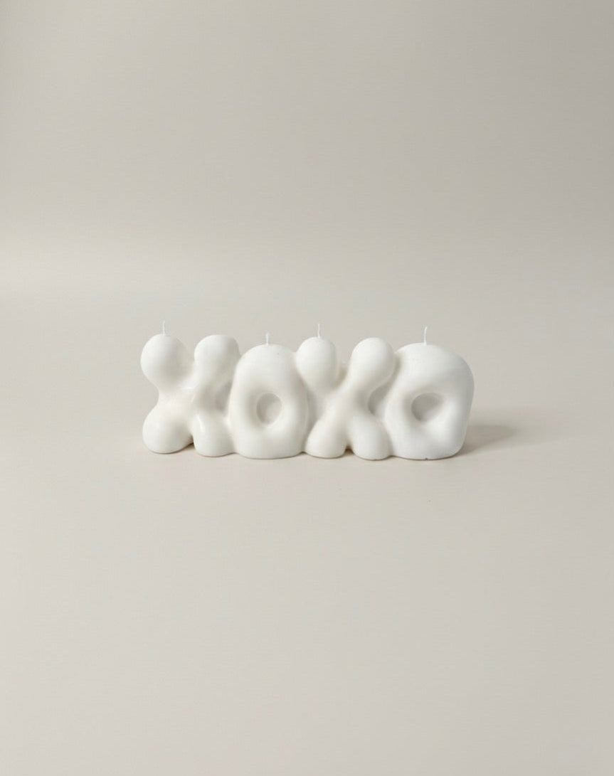 White 'XOXO' candle on a beige background