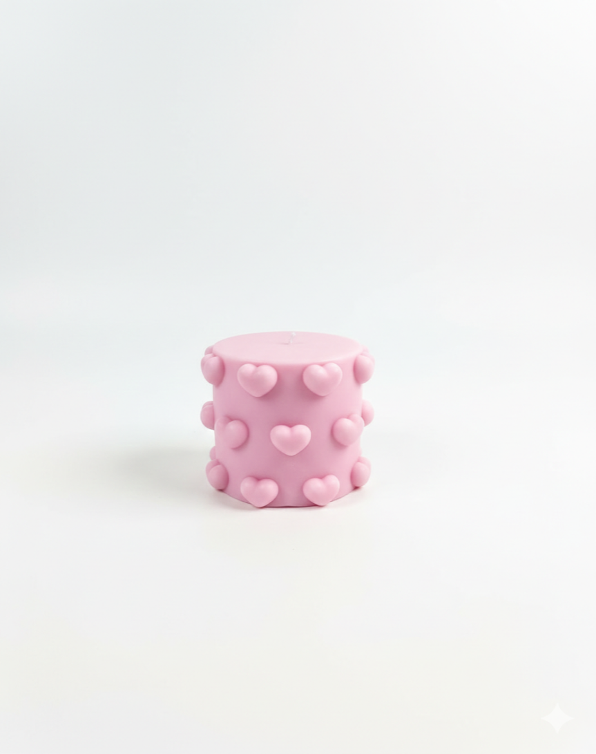Pink cylindrical candle with heart patterns on a white background